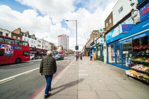 Uma rua com um ônibus de dois andares vermelho, um homem caminhando na calçada e uma loja com uma placa azul anunciando carne e peixe halal.