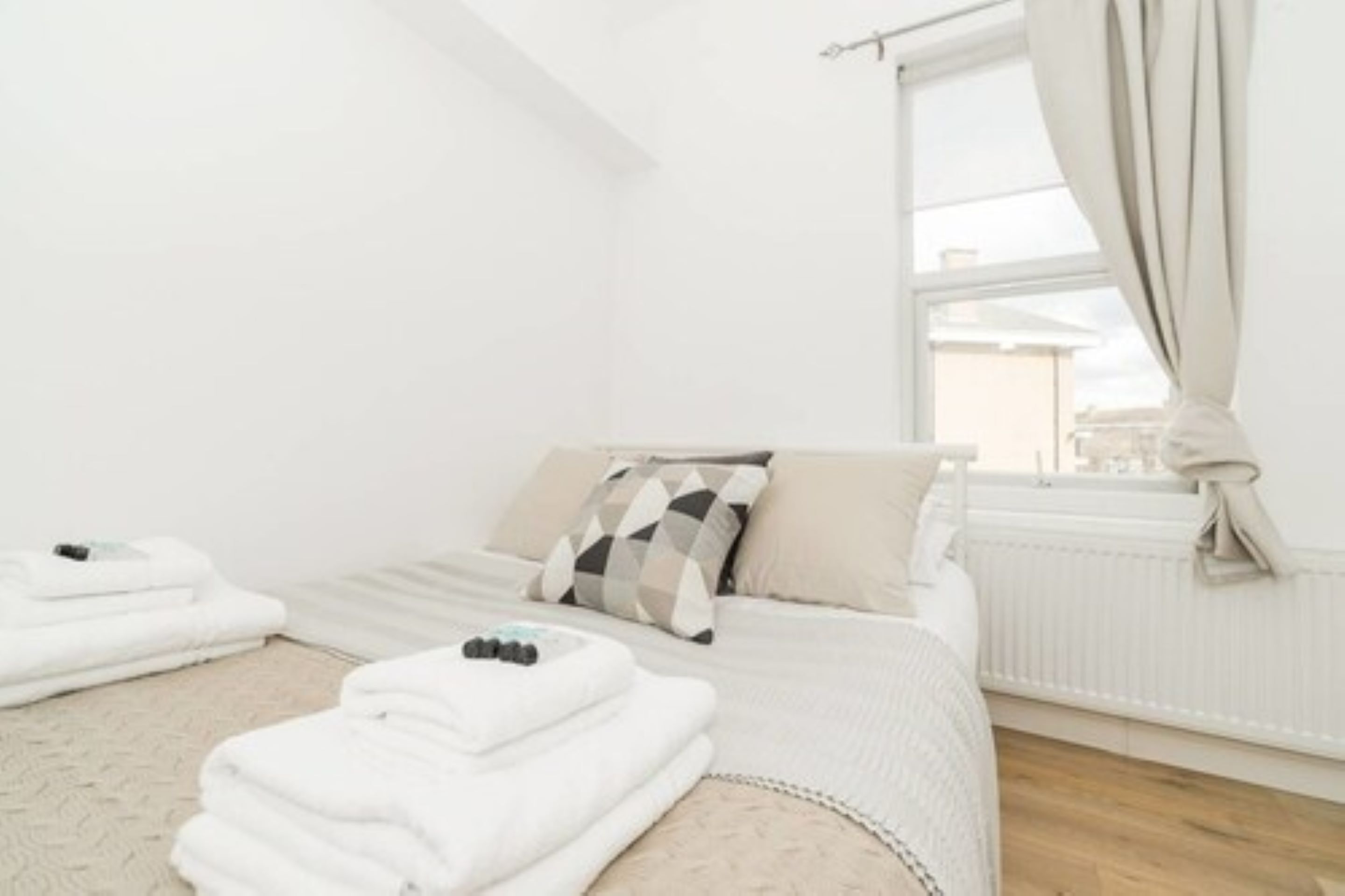 A clean, white hotel room with a bed, a window with curtains, and a radiator.