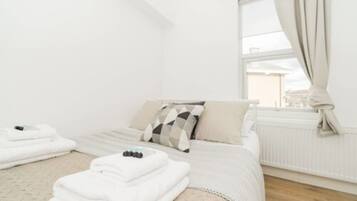 A clean, white hotel room with a bed, a window with curtains, and a radiator.