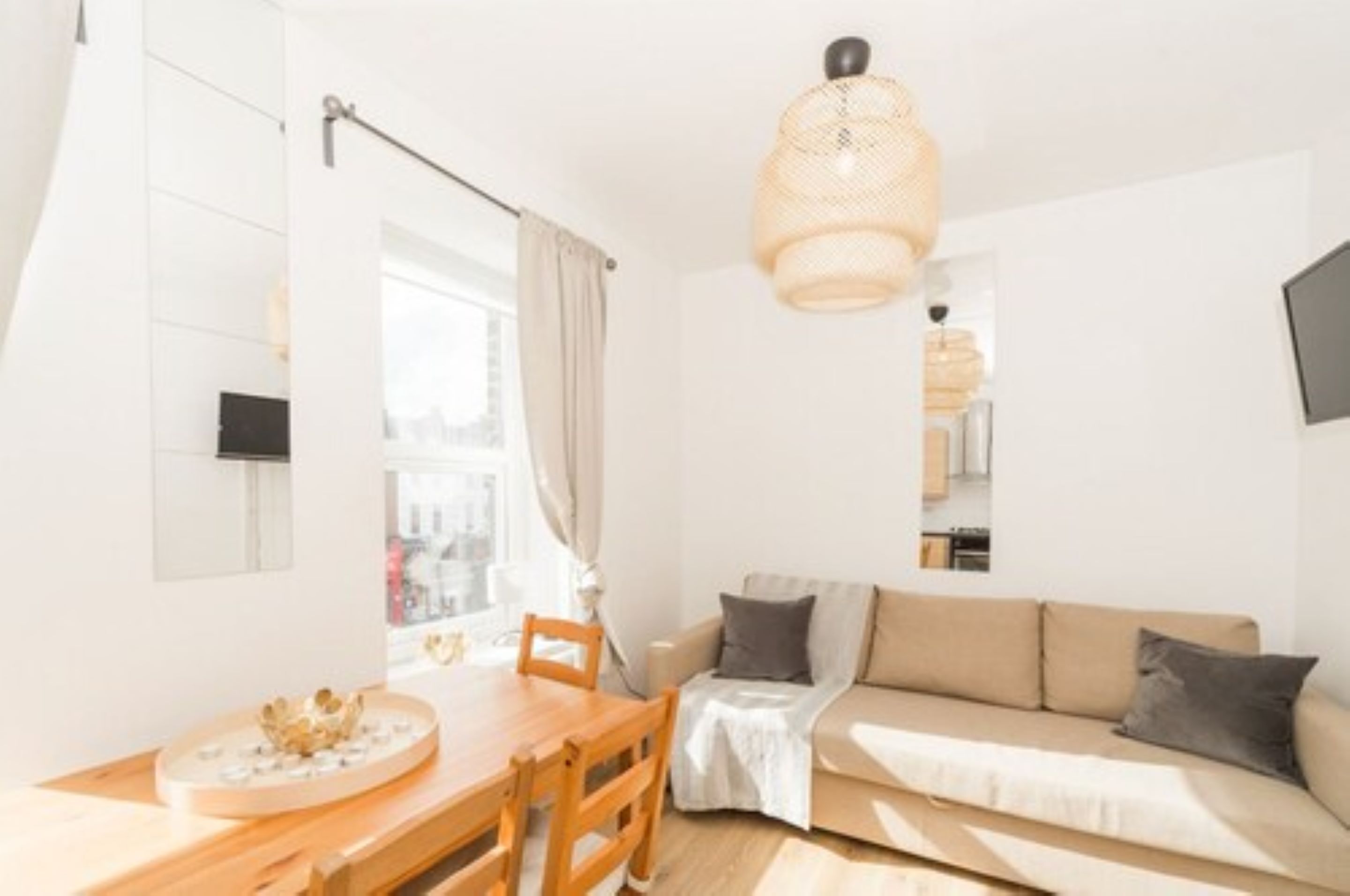 A bright living room with a wooden dining table, a beige sofa, and a hanging light fixture.