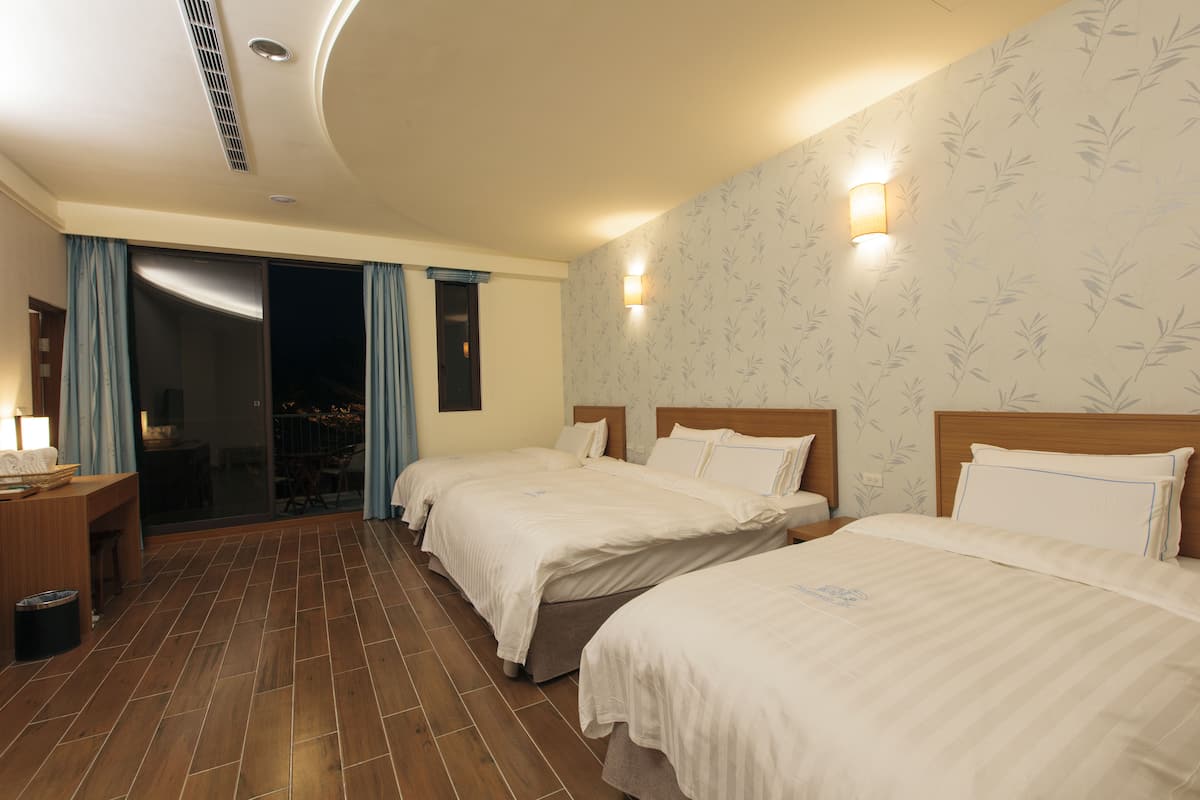 A hotel room with two beds, a desk, and a sliding glass door leading to an outdoor area.