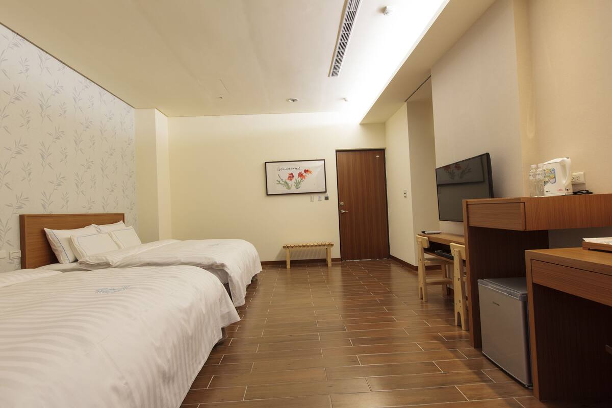 A hotel room with two beds, a desk, a television, and a mini-fridge.