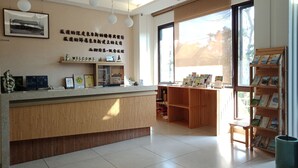 A reception area with a wooden counter, a welcome sign, a framed picture, and a bookshelf with books. - Footprint Inn (Jiji)