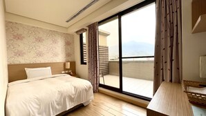 A hotel room with a bed, a bedside table, a mirror, a window with curtains, and a view of the mountains. - Footprint Inn (Jiji)