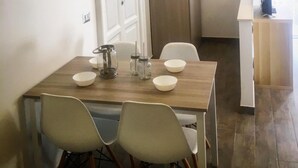 A dining area with a wooden table and four chairs, a white door, and a view of a kitchen area. - EmyJo Central B&B (Naples)