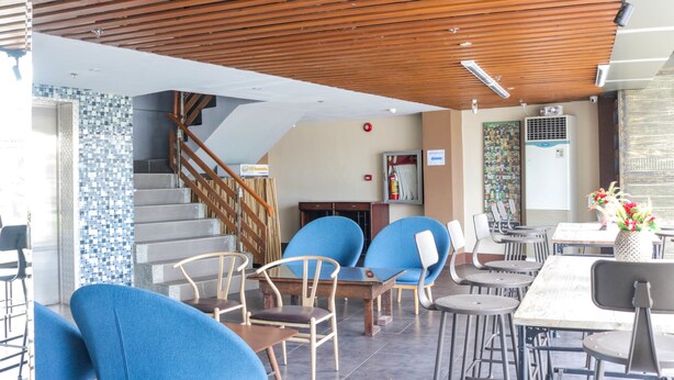 A modern outdoor seating area with wooden ceiling, blue chairs, and a staircase leading to an upper level. - RedDoorz Plus near UV Mandaue Cebu (Mandaue)