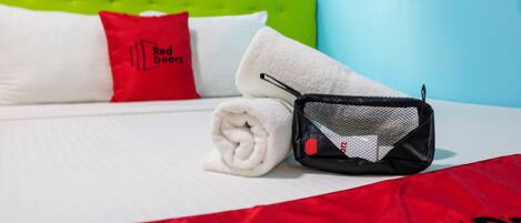 Ein ordentlich bezogenes Bett mit einem weißen Kissen, einem roten Kissen mit dem Aufdruck 'Red Door' und einem aufgerollten weißen Handtuch.