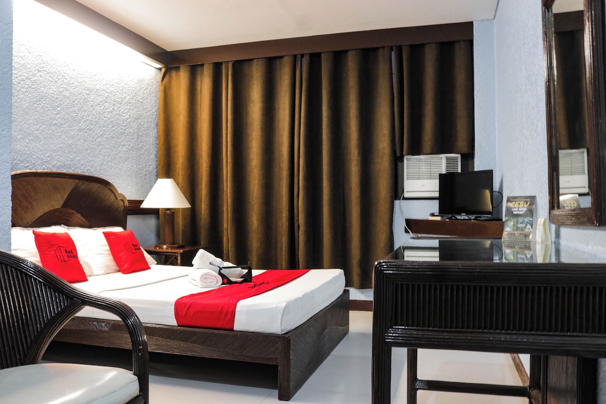 A hotel room with a bed, a desk, a chair, a TV, and curtains.