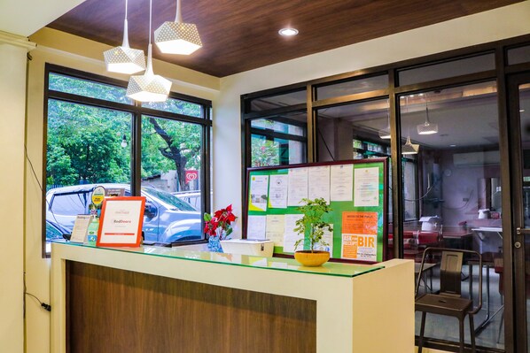 A reception desk with a glass top, wooden paneling, and a view of parked cars outside. - RedDoorz @ Junquera Extension Cebu (Cebu City)