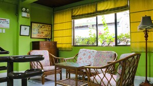 Una habitación con paredes verdes, techo de madera, una mesa, cuatro sillas de mimbre, una lámpara y un ventanal con cortinas amarillas.