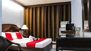 Una habitación de hotel con cama, escritorio, silla, televisor y cortinas.