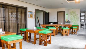 Un comedor de hotel con mesas de madera y bancos acolchados verdes, un ventanal con cortinas y un cuadro colgado en la pared.