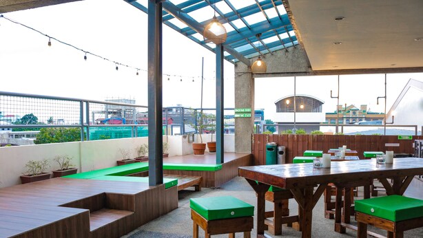 Un patio al aire libre con mesas y bancos de madera, plantas en macetas y vista de la ciudad.
