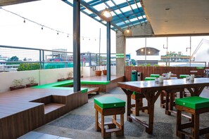 An outdoor patio area with wooden tables and benches, potted plants, and a view of the cityscape. - RedDoorz @ Junquera Extension Cebu (Cebu City)