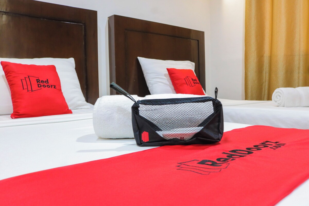 A hotel room with a neatly made bed, two pillows with the Red Doorz logo, a white towel, and a red towel on the bed.