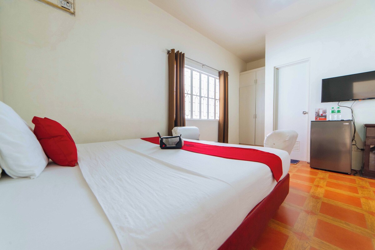 A hotel room with a bed, a desk, a chair, a television, and a window with curtains.