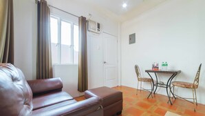 Una habitación con un sofá de cuero marrón, una mesita con dos sillas y una ventana con cortinas.