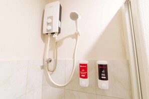 A bathroom with a wall-mounted shower, a handheld showerhead, and two dispensers for RedDoor's conditioning shampoo and body wash.