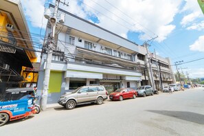 A multi-story building with a ground-level commercial space, parked cars, and a tuk-tuk on the street.