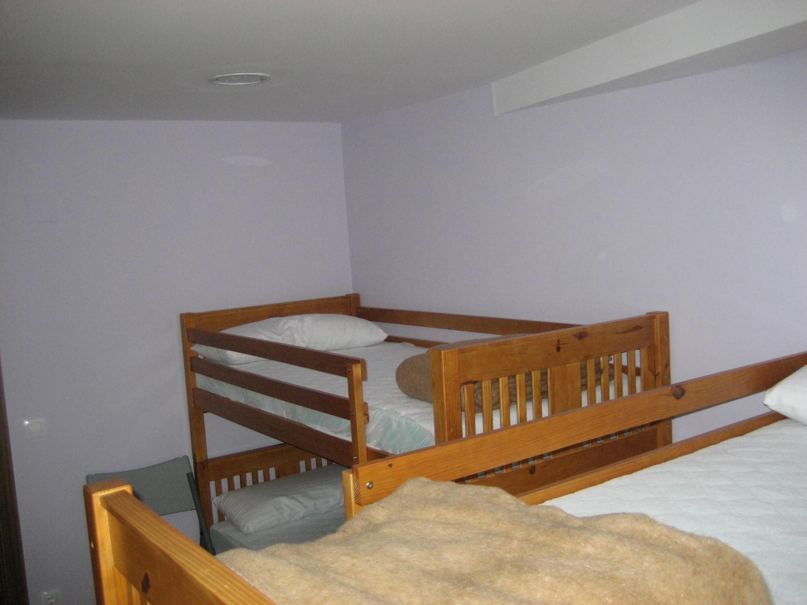 Una cama litera con una cama inferior y una cama individual, ambas con estructura de madera y ropa de cama blanca.