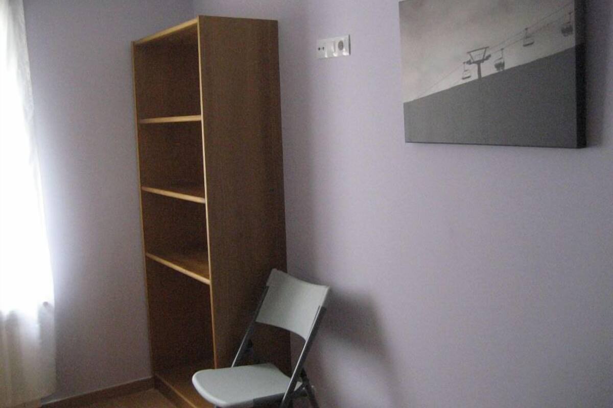 A room with a wooden wardrobe, a grey chair, and a painting on the wall.