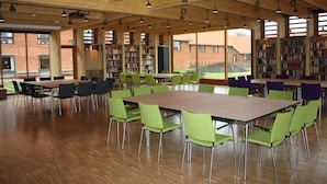 Una biblioteca amplia con techos de madera, sillas verdes y moradas, y estanterías llenas de libros.