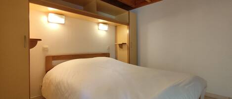 A single bed with a wooden headboard in a room with a sloped ceiling and two wall-mounted light fixtures.
