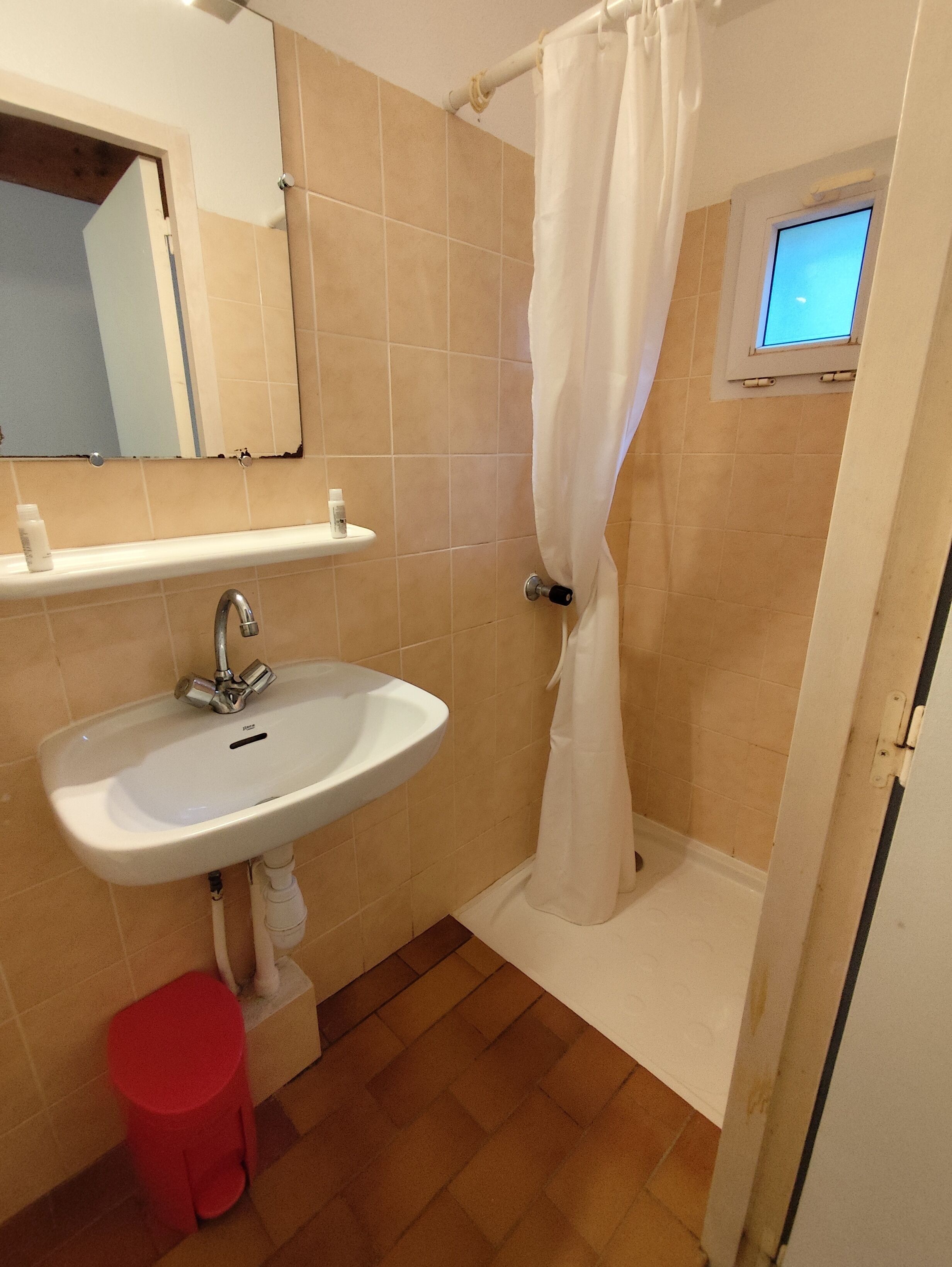Een badkamer met een wastafel, spiegel, douchegordijn en een klein raam.