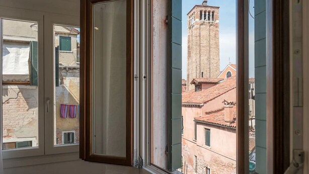 A room with a large window overlooking a historic building with a bell tower. - Ca' Dandolo (Venice)