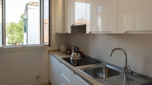 A kitchen with white cabinets, a stainless steel sink, and a window with a view of buildings and trees. - Ca' Dandolo (Venice)