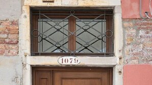 A wooden double door with a metal window grille above it, and the number 1079 on the door. - Ca' Dandolo (Venice)