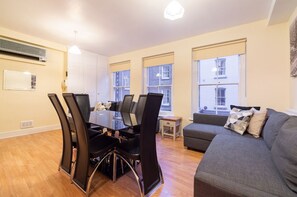 A modern living room with a glass dining table surrounded by chairs, a grey sofa, and a small side table. - PML Apartments Soho (London)