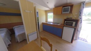 A compact kitchen with a gas stove, microwave, and a small refrigerator. There is a dining table with chairs and a bed in the adjacent room. - Las Casitas de Las Arribes (Aldeadavila de la Ribera)