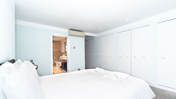 A modern hotel room with a large bed, a wardrobe with multiple doors, and a bathroom visible through an open door. - PML Apartments Notting Hill (London)