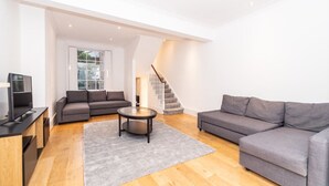 A modern living room with a grey sofa, a round coffee table, and a staircase leading to an upper level. - PML Apartments Notting Hill (London)