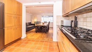 A modern kitchen with wooden cabinets, a dining area with a table and chairs, and a visible stove. - PML Apartments Notting Hill (London)