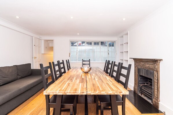 A dining area with a wooden table, black chairs, a grey sofa, and a fireplace.