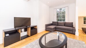 A modern living room with a flat-screen TV, a sectional sofa, and a glass coffee table. - PML Apartments Notting Hill (London)