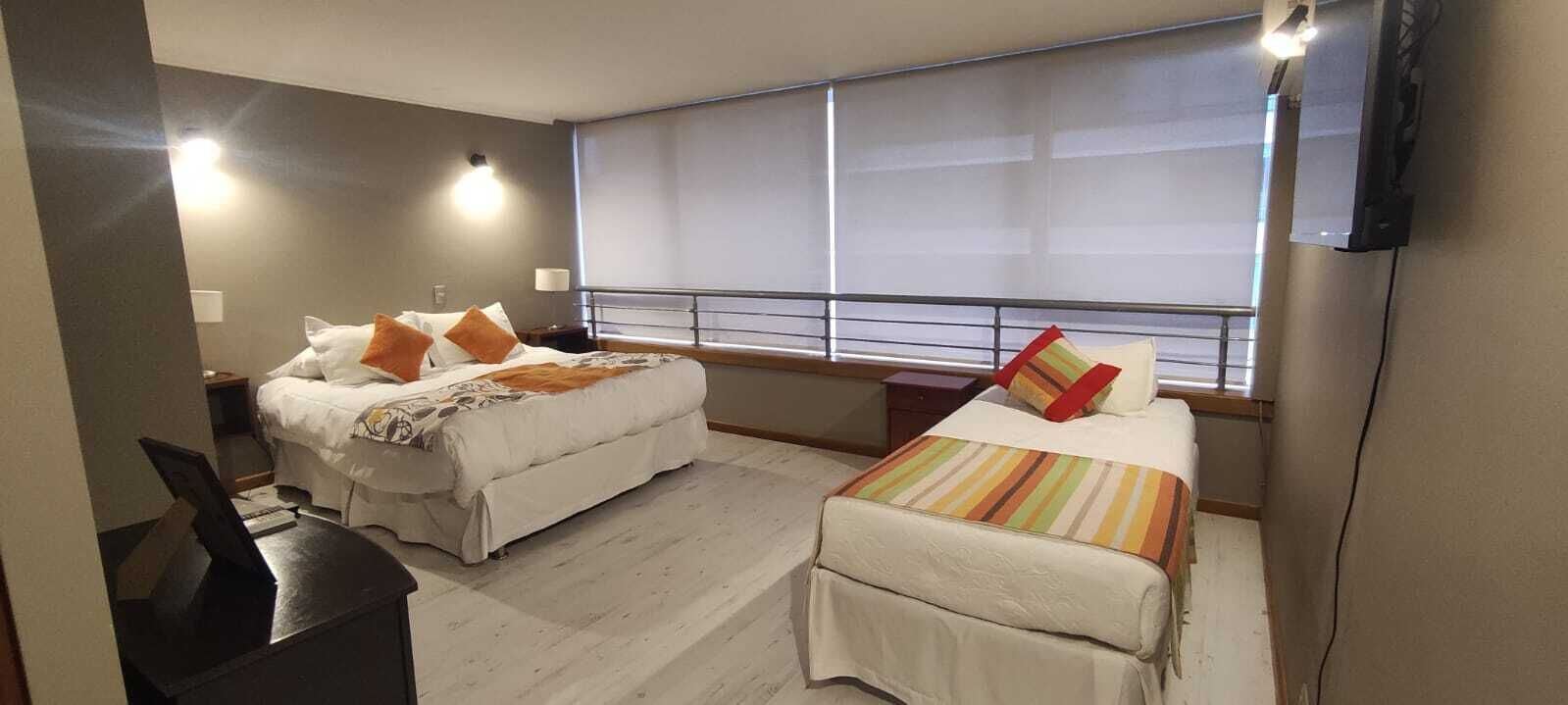 A hotel room with two beds, a desk, and a large window.