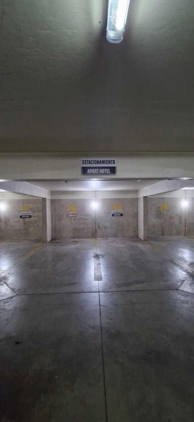 Un parcheggio sotterraneo con pareti in cemento e una luce al soffitto. Un cartello indica 'ESTACIONAMIENTO APART HOTEL'.