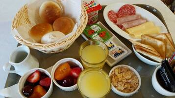 A breakfast tray with bread rolls, sliced meats, cheese, and pastries.
