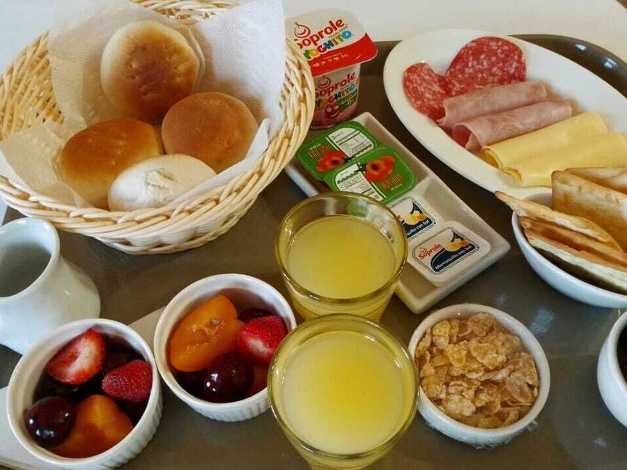 A breakfast tray with bread rolls, sliced meats, cheese, and pastries.