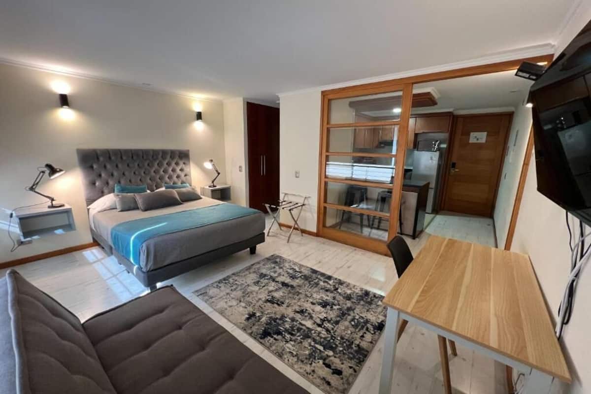 A bedroom with a bed, bedside tables, a desk, and a TV.