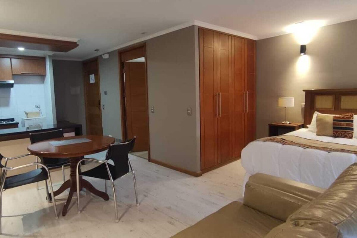 A hotel room with a bed, a sofa, a dining area with a table and chairs, and a kitchen area.