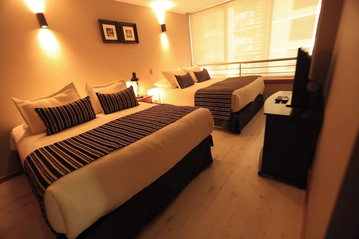 A hotel room with two beds, a desk, and a TV.