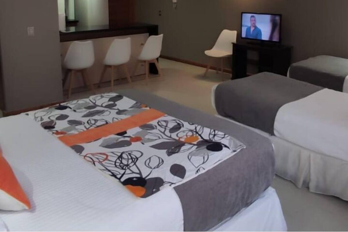 A hotel room with a bed, a TV, a desk with chairs, and a kitchenette.