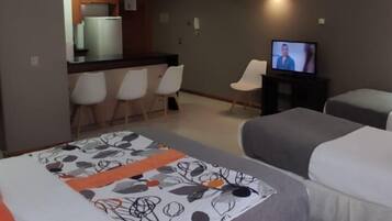 Habitación de hotel con cama, televisión, escritorio con sillas y kitchenette.