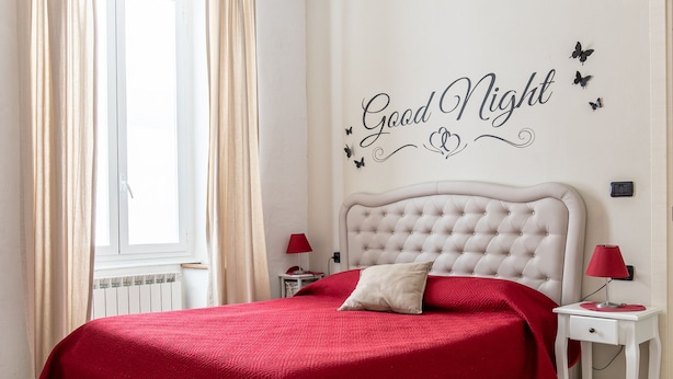 A bedroom with a bed, a nightstand, a window with curtains, and a wall with a 'Good Night' sign. - Sapore di mare 5 Terre Affittacamere (La Spezia)