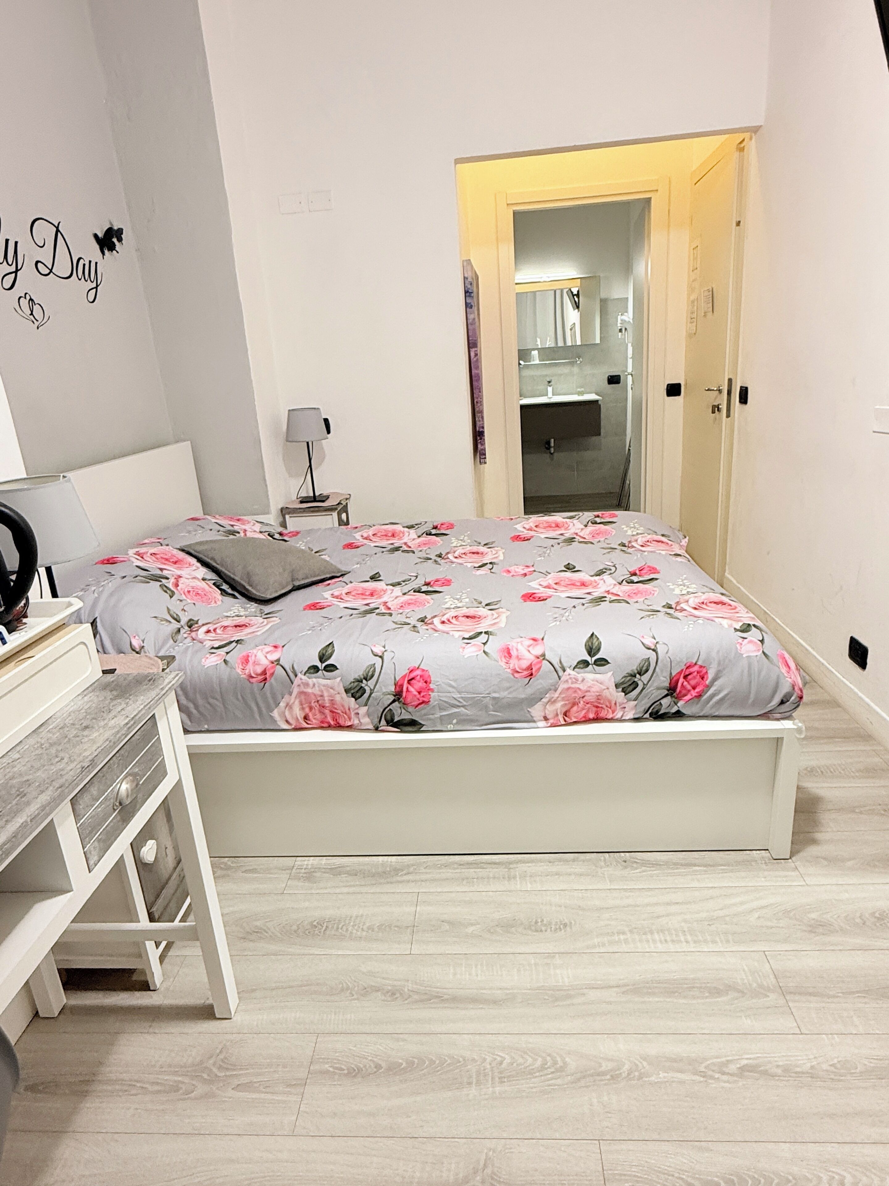 Una camera da letto con un letto, un comodino, una lampada e una scrivania con cassetti.