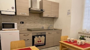 A compact kitchen with a microwave, oven, and sink. There is a dining table with chairs and a red placemat. - Sapore di mare 5 Terre Affittacamere (La Spezia)